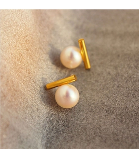 Detail of elegant gold tube pearl earrings on a textured grey background