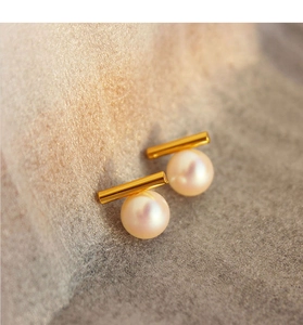 Close-up of elegant minimalist pearl earrings with a gold bar and iridescent white pearl