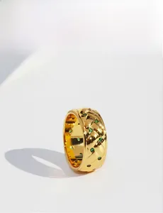 Detailed view of wide gold quilted ring with green emerald-like small gemstones