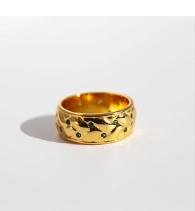 Macro shot of gold wide ring featuring quilted pattern and green zircon inlay
