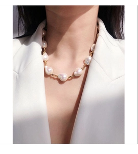 Dettaglio della collana di perle barocche e sfere dorate su un blazer bianco