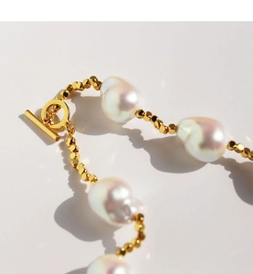 Dettaglio collana di perle barocche con perline sfaccettate dorate e chiusura T-bar