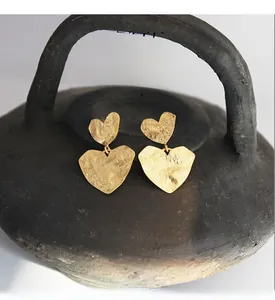 Detail of gold-plated brass heart earrings with hammered texture and cubic zirconia