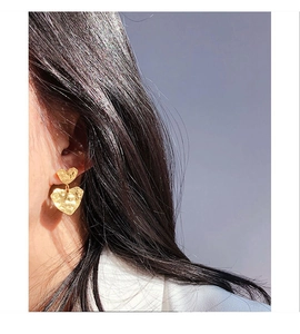 Close-up of heart-shaped gold earrings with hammered texture on a model's ear