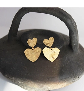 Detail of golden heart earrings with hammered texture hanging on a ceramic pot edge
