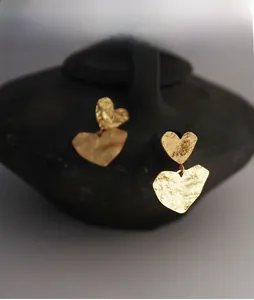 Detail shot of golden double heart earrings with hammered texture on ceramic stand