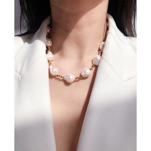 Collana di perle barocche con perle dorate indossata da una modella in blazer bianco
