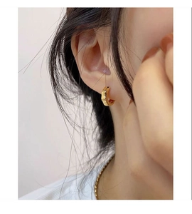 Close-up of gold-plated bamboo texture hoop earrings worn on a model's ear