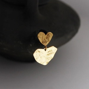 Golden double heart drop earrings with vintage hammered metal texture on black pottery