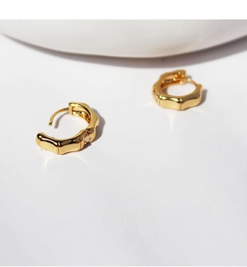 Macro detail of gold-plated bamboo texture hoop earrings with polished metal finish