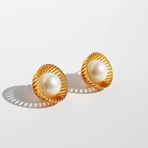 Boucles d'oreilles cage dorée évidée avec perles blanches et ombre sur fond blanc
