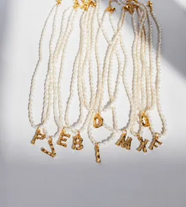 Detalle de colgantes de letras doradas con circonitas en collar de perlas naturales