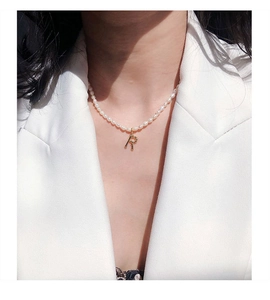 Primer plano de collar de perlas naturales con un colgante de la letra R en oro