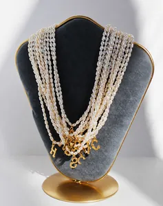 Detalle de collar de perlas de agua dulce con colgantes de letras doradas en terciopelo