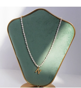 Detalle de collar de perlas de agua dulce con colgante de letra N dorada y texturizada