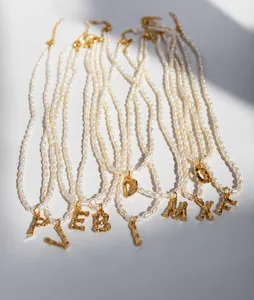 Detalle de collares de perlas de agua dulce con colgantes de letras doradas texturizadas