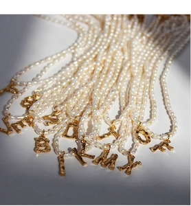 Detalle de collares de perlas de agua dulce con colgantes de letras doradas estilo bambú