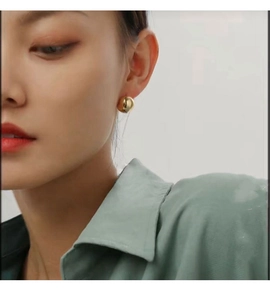 Close-up of a model wearing a minimalist gold-polished hollow spherical stud earring