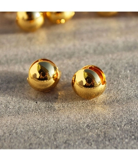 Detailed close-up of high-polish gold hollow spherical hoop earrings on stone