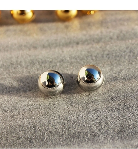 Close-up of minimalist polished silver spherical earrings on a textured grey surface