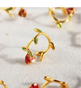 Macro view of gold vine ring with a red enamel rosebud and green leaf detailing