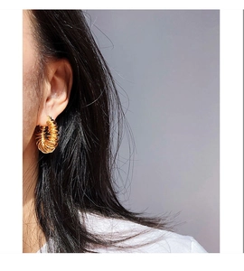 Close-up of golden spiral loop earrings on ear showing textured brass metal design
