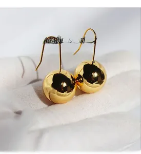 Detailed view of large polished golden ball drop earrings held in a white gloved hand