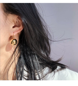 Close-up of a polished golden mirror ball drop earring worn by a female model