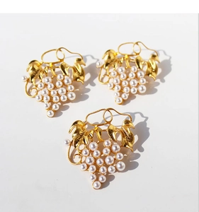 Detailed view of grape-shaped gold-plated brooches featuring white pearls and leaf motifs