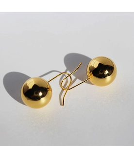 Detail of polished golden ball earrings with smooth mirror finish and hook design