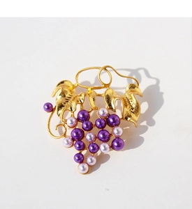 Macro detail of gold-plated leaf textures and purple pearl grape cluster on the brooch
