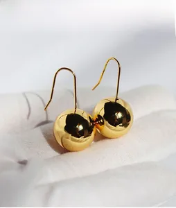 Macro shot of mirror-polished gold sphere earrings being held with a white glove