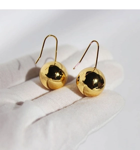 Detailed view of large gold mirror-finish spherical earrings held by a gloved hand
