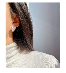 Close-up of heart-shaped earring with pink and green stones on model's ear