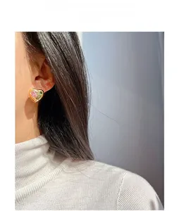 Detail showing heart-shaped gold earring with pink and green zircon stones on ear