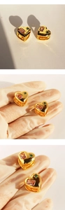 Close-up of golden heart earrings with pink rectangular gemstone and green star accent