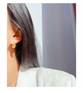 Close-up of gold-plated huggie earrings with zircon starburst pattern on model's ear