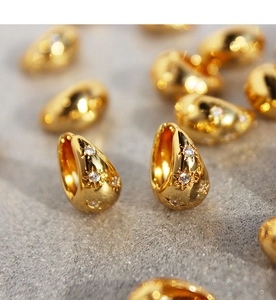 Macro shot of gold teardrop earrings featuring engraved stars and zircon stone details