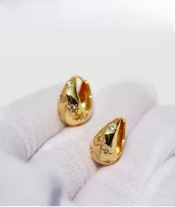 Detail of chunky gold drop hoops with starburst zircon settings on white glove