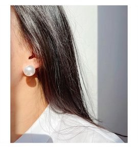 Close-up of a large round white pearl earring worn by a model in minimalist natural light