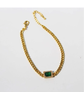 Macro view of gold-plated curb chain bracelet featuring a green emerald zircon stone