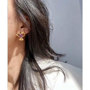 Orecchini a fiore dorati con zircone viola indossati da una modella primo piano