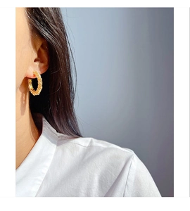 Detail of golden textured C-shape hoop earring worn by a model in elegant white shirt