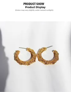 Macro detail of golden C-shape earrings with irregular hammered lava texture surface