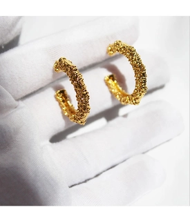 Close-up of golden C-shaped earrings with irregular hammered texture and vintage finish
