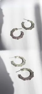 Close-up of C-shaped earrings showing detailed irregular hammered texture and metallic finish