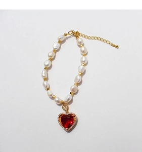 Dettaglio del bracciale di perle con gemma a cuore rosso e chiusura dorata