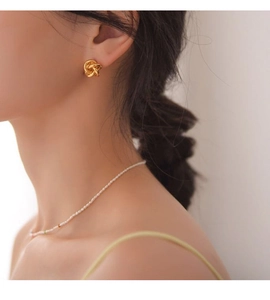 Gros plan d'un mannequin portant des boucles d'oreilles nœuds minimalistes dorées