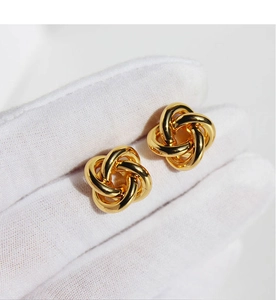 Détail de boucles d'oreilles nœud d'amour plaqué or poli tenues par une main gantée sur blanc