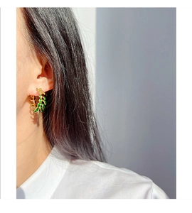 Close-up of C-shaped leaf earrings with green enamel on a model's ear in natural light
